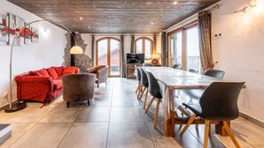 A dining area with a long wooden table, black chairs, a red sofa, and a fireplace.