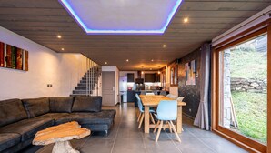 Un interior moderno con techo de madera, un comedor con mesa y sillas de madera, un sofá de cuero y una escalera que conduce a un nivel superior.