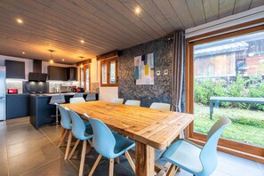 Une cuisine moderne avec des meubles en bois, un îlot central et un coin repas comprenant une table en bois et des chaises bleues.