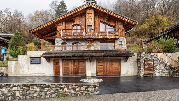 Una cabaña con fachada de piedra, balcones de madera y una escalera de piedra.