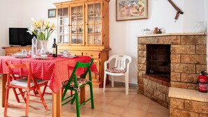 A dining area with a table set for two, a wooden cabinet, a fireplace, and a television.