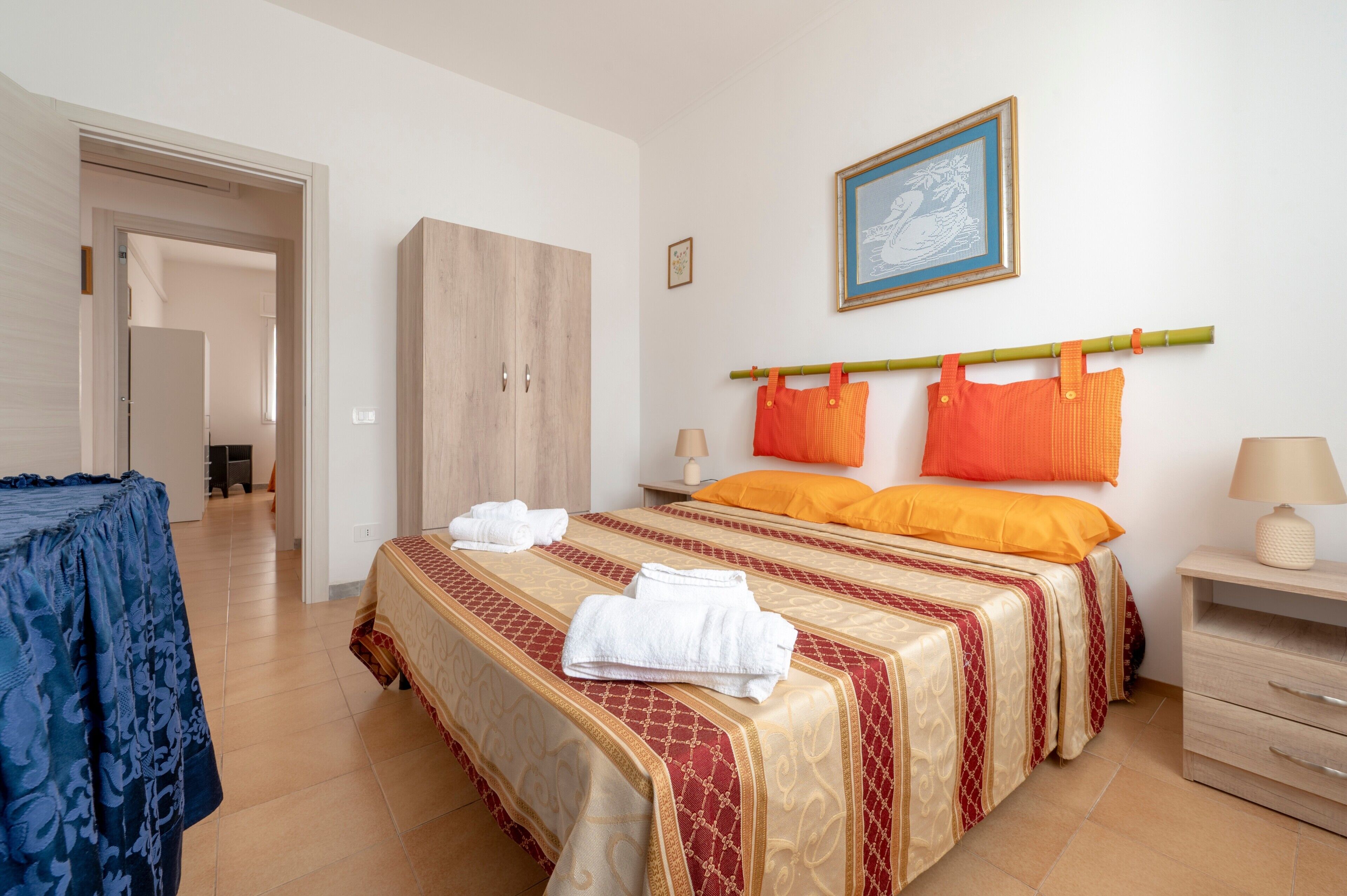 A hotel room with a bed, a wardrobe, a nightstand, a lamp, and a framed picture on the wall.