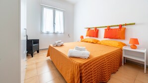 A bedroom with a bed, two pillows, a nightstand, a lamp, a window, and a chair.
