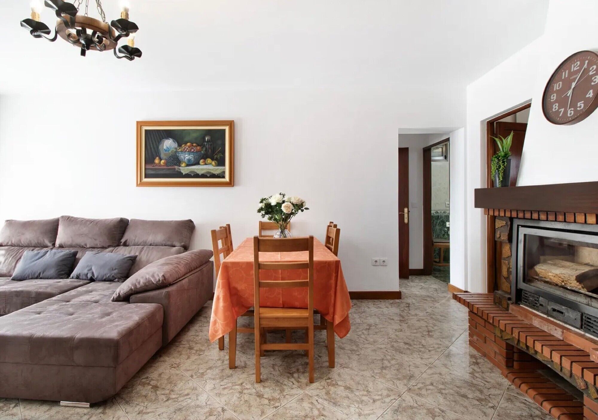 Un salon comprenant un canapé, une table à manger avec des chaises, une cheminée, une horloge et un tableau encadré accroché au mur.