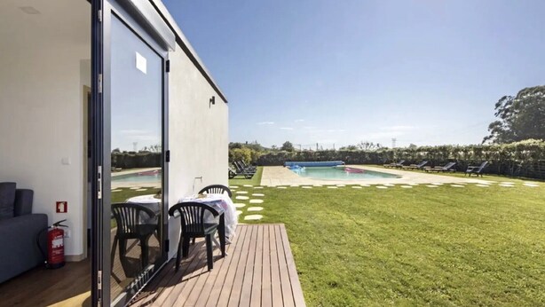 A modern building with a pool, a grassy deck, and outdoor seating.