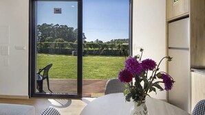 A room with a large sliding glass door leading to a grassy outdoor area, a white table with a vase of flowers, and a houndstooth-patterned chair.