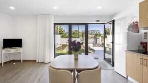 A modern room with a TV, a dining table with chairs, a kitchen area, and a sliding glass door leading to an outdoor area.