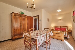 Une pièce comprenant une table à manger en bois, des chaises, un lit avec une tête de lit, des tables de chevet, une armoire et un lustre.