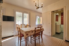 A dining area with a table, chairs, a chandelier, and a view through a door to a kitchen.