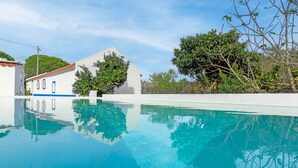 A swimming pool with clear water, surrounded by a white building with blue trim and a tree with green foliage.