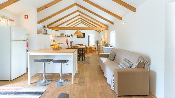 A spacious kitchen with wooden beams, a dining area, and a living room with a sofa.