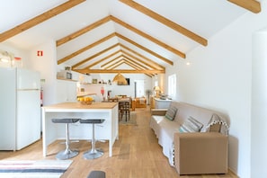 A spacious kitchen with wooden beams, a dining area, and a living room with a sofa.