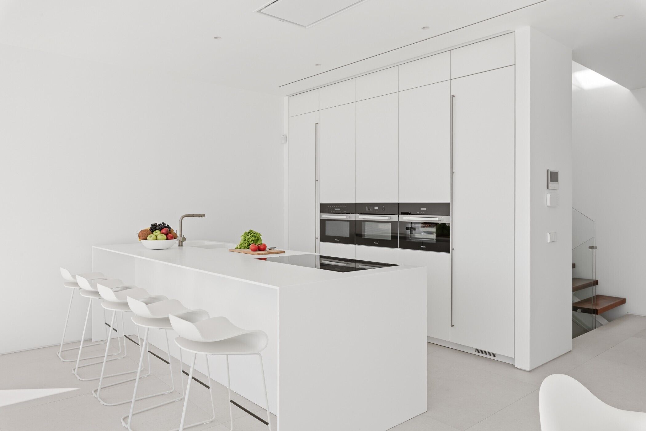 A modern kitchen with white cabinetry, a central island with bar stools, and a built-in oven.