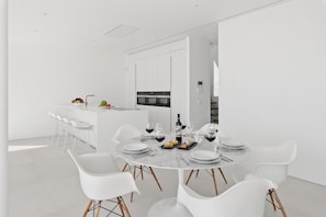 Een moderne keuken met witte kasten en een eethoek met een marmeren tafel en witte stoelen.
