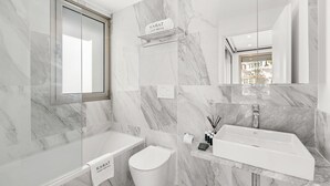 Une salle de bain moderne avec une baignoire, des toilettes et un lavabo, des murs en marbre et une fenêtre.