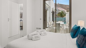 Une chambre d’hôtel moderne avec un grand lit, deux serviettes portant la marque « Karat », un balcon avec une table et des chaises, et une vue sur la montagne.