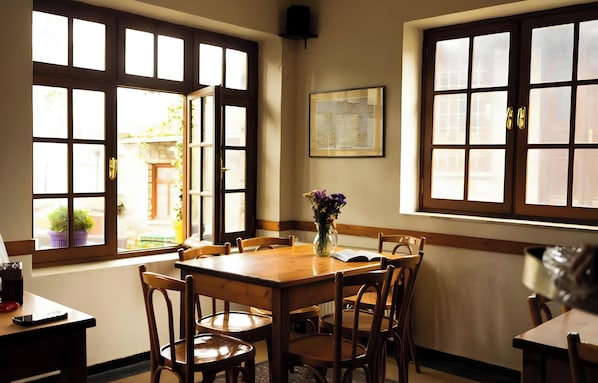 Un coin repas avec une table et des chaises en bois, de grandes fenêtres à carreaux et un vase rempli de fleurs posé sur la table.