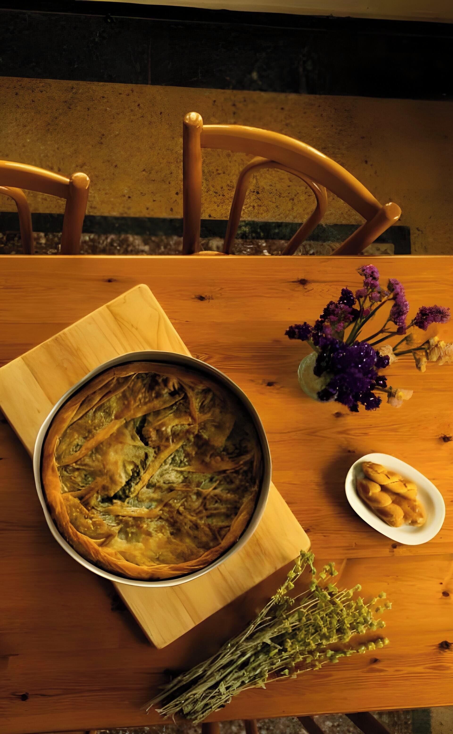 Ein Holztisch mit einer Torte, einer kleinen Brotschale und einer Blumenvase.