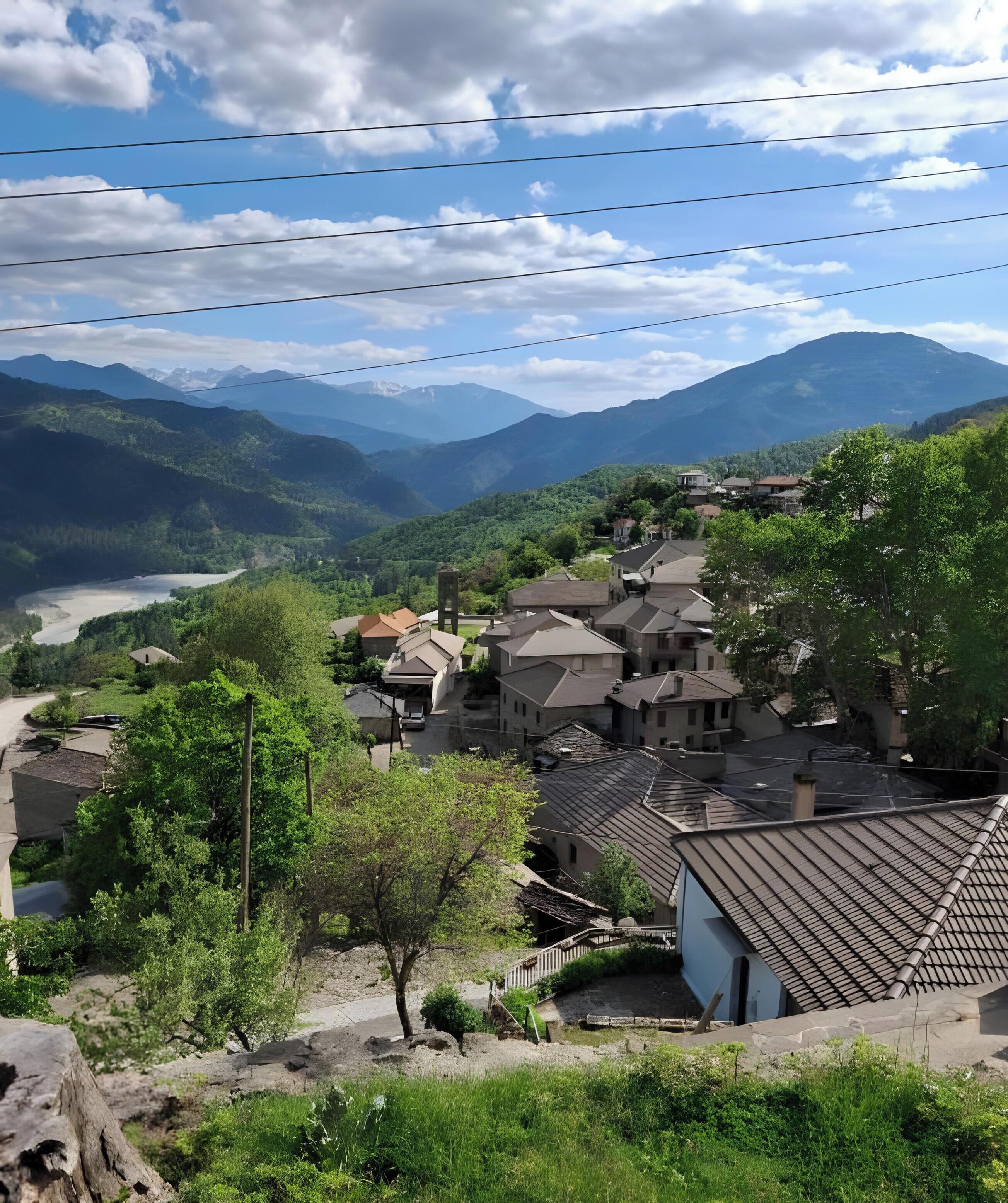 A village with traditional buildings, a river, and mountains in the background.