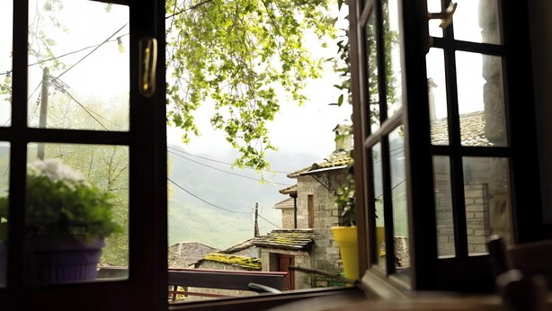 A window with a view of a stone building, a potted plant, and a hanging light fixture. - Guest House 'Armoloi Room 2' with Mountain View, Shared Terrace and Wi-Fi (Konitsa)