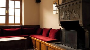 Una habitación con un banco de madera, una chimenea con adornos decorativos y un ventanal de varios cristales.