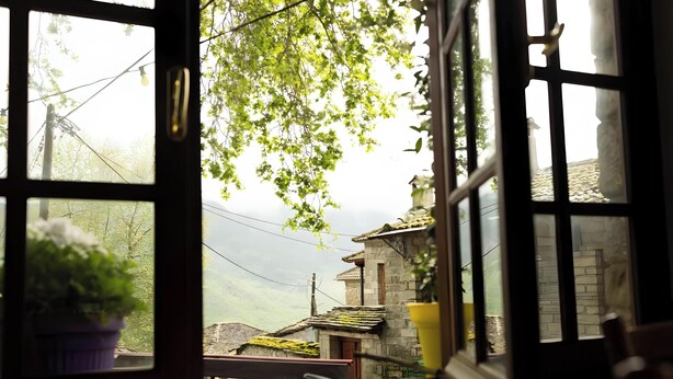 Una ventana con vista a un edificio de piedra, una planta en maceta y una lámpara colgante.