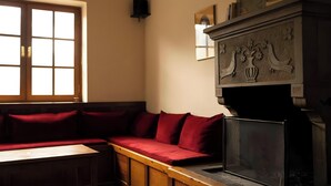 A room with a wooden bench, a fireplace with decorative carvings, and a window with multiple panes.