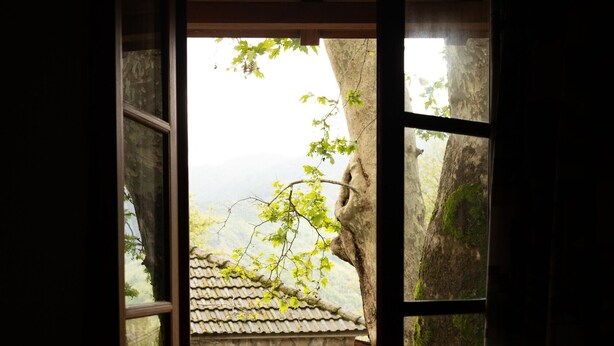 A wooden-framed window with a view of a stone building and a tree.