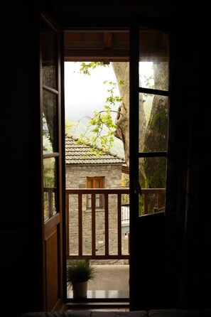 Una ventana de madera con vista a un edificio de piedra y un árbol.