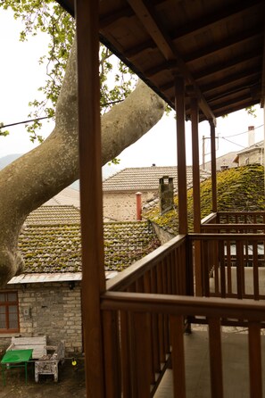 A wooden balcony with a stone wall and a large tree in the background. - Guest House 'Armoloi Room 6' with Mountain View, Shared Terrace and Wi-Fi (Konitsa)
