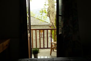 A room with a bed, a wooden chair, a potted plant, and a view of a traditional building outside.