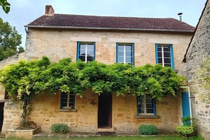 Un edificio de piedra con techo de tejas, tres ventanas con contraventanas azules y una pared cubierta de hiedra.
