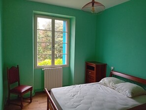 A room with a bed, a chair, a radiator, and a window with a view of greenery.