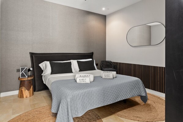 Une chambre d’hôtel moderne, équipée d’un lit, d’une table d’appoint ronde en bois, d’un miroir et d’un luminaire fixé au mur.