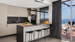 Une cuisine moderne dotée d’un grand îlot central, de tabourets de bar et offrant une vue sur la ville grâce à de grandes fenêtres.