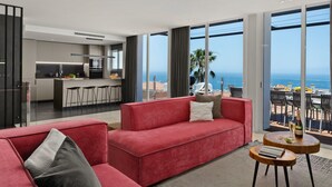 Un salon moderne avec un canapé rouge, une petite table en bois et une vue sur l’océan.