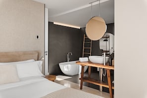 Ein modernes Schlafzimmer mit einem Bett, einem Nachttisch, einem Holzbeistelltisch, einem runden Spiegel, einer weißen Badewanne und einer Holzkommode mit Waschbecken.