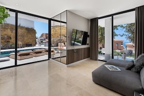 Ein modernes Wohnzimmer mit großem Fernseher, bequemen Sitzgelegenheiten und Blick auf Pool und Außenbereich.