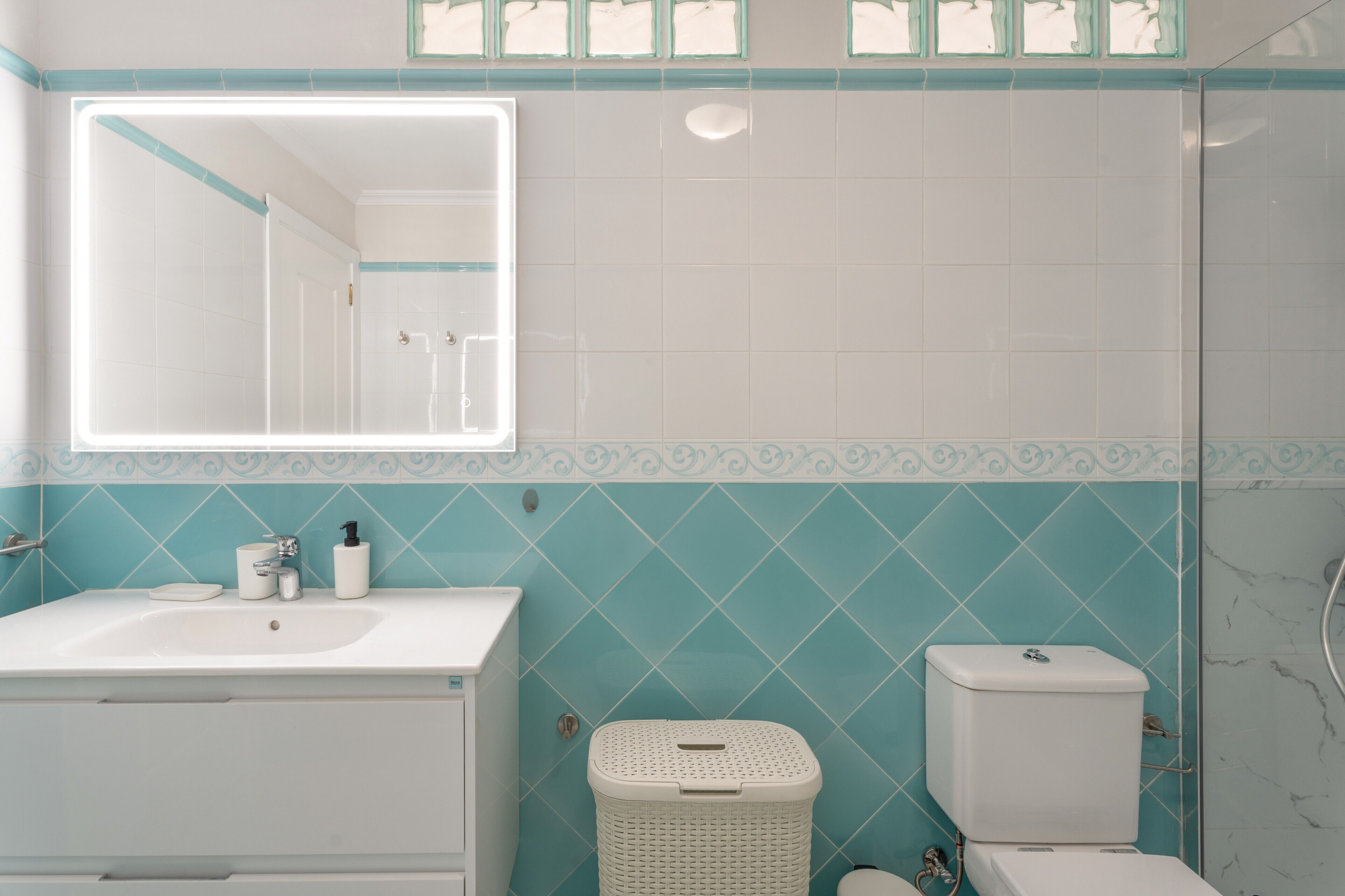 A bathroom with a sink, mirror, toilet, and a laundry basket.