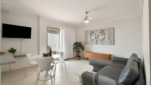 Una sala de estar moderna con un televisor de pantalla plana, un sofá gris, una mesa de comedor con sillas y una planta en maceta.