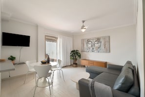 Una sala de estar moderna con un televisor de pantalla plana, un sofá gris, una mesa de comedor con sillas y una planta en maceta.