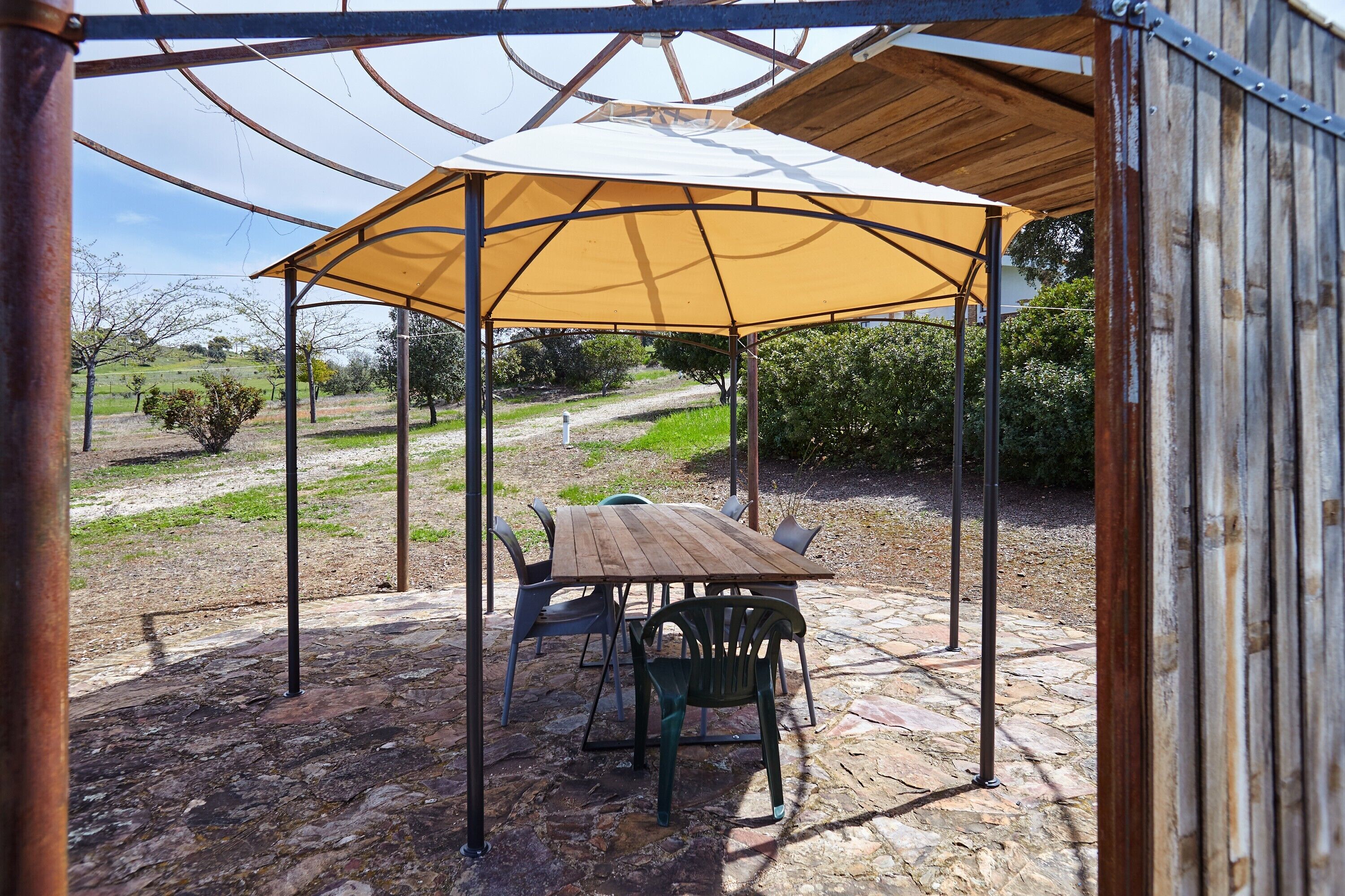 Un espace extérieur abrité, doté d’une table et de chaises, entouré d’un sol en pierre et d’une structure en métal.