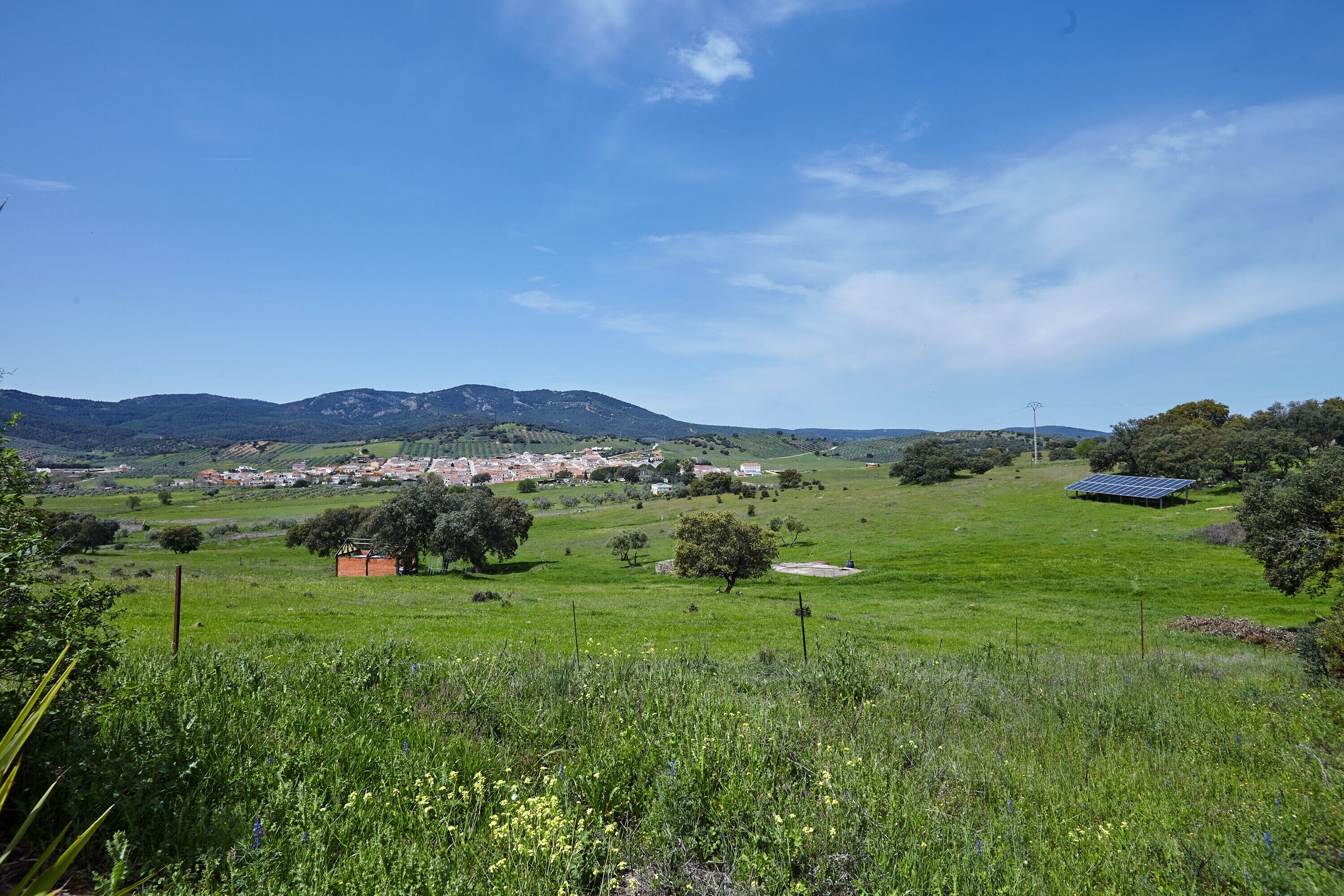 Paisatge rural amb un poble, camps verds i muntanyes al fons.