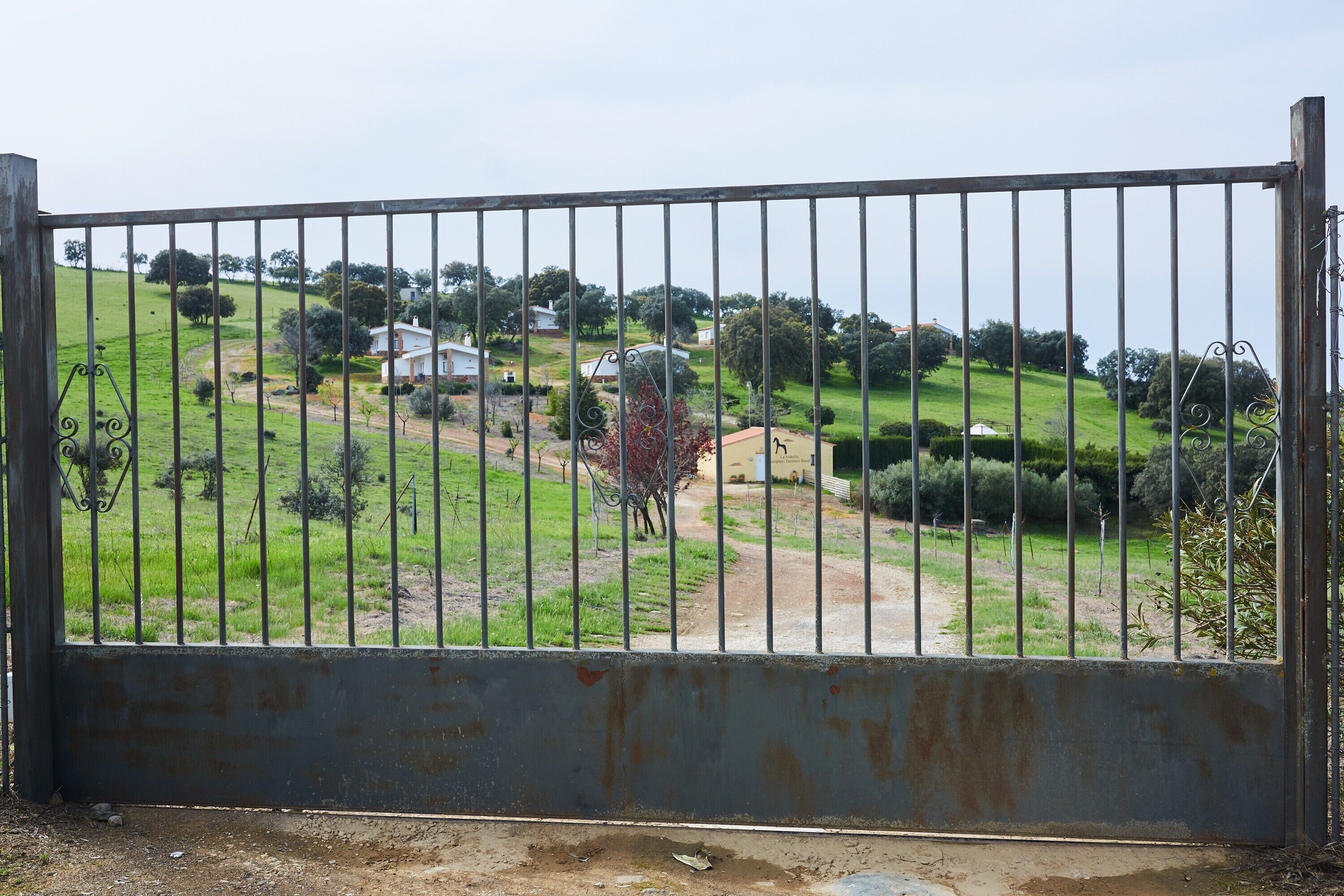Una propiedad amurallada con un sendero de tierra que lleva a una casa rodeada de vegetación.