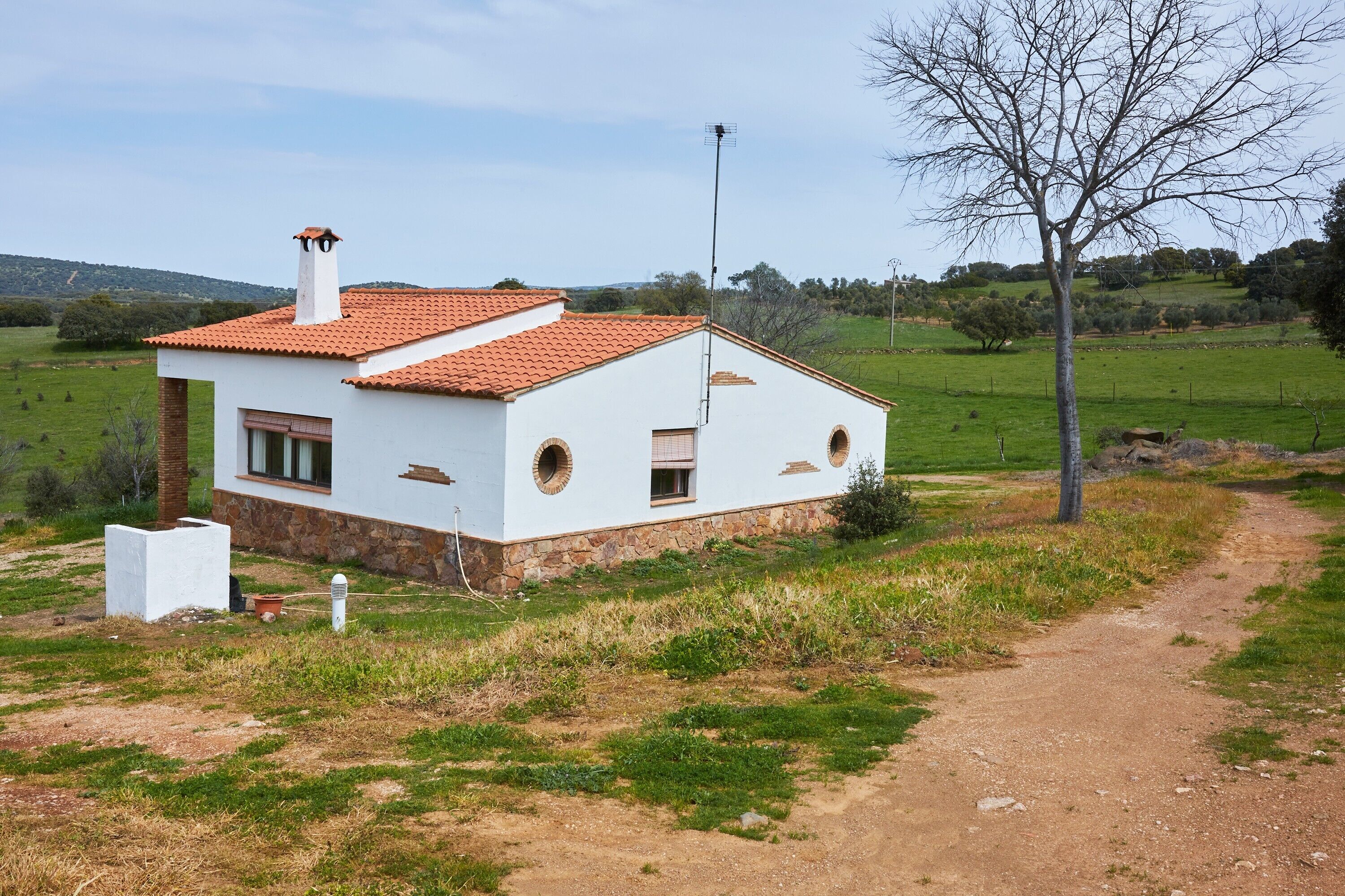 Una casa blanca con techo de tejas rojas, una chimenea y un ventanal pequeño.
