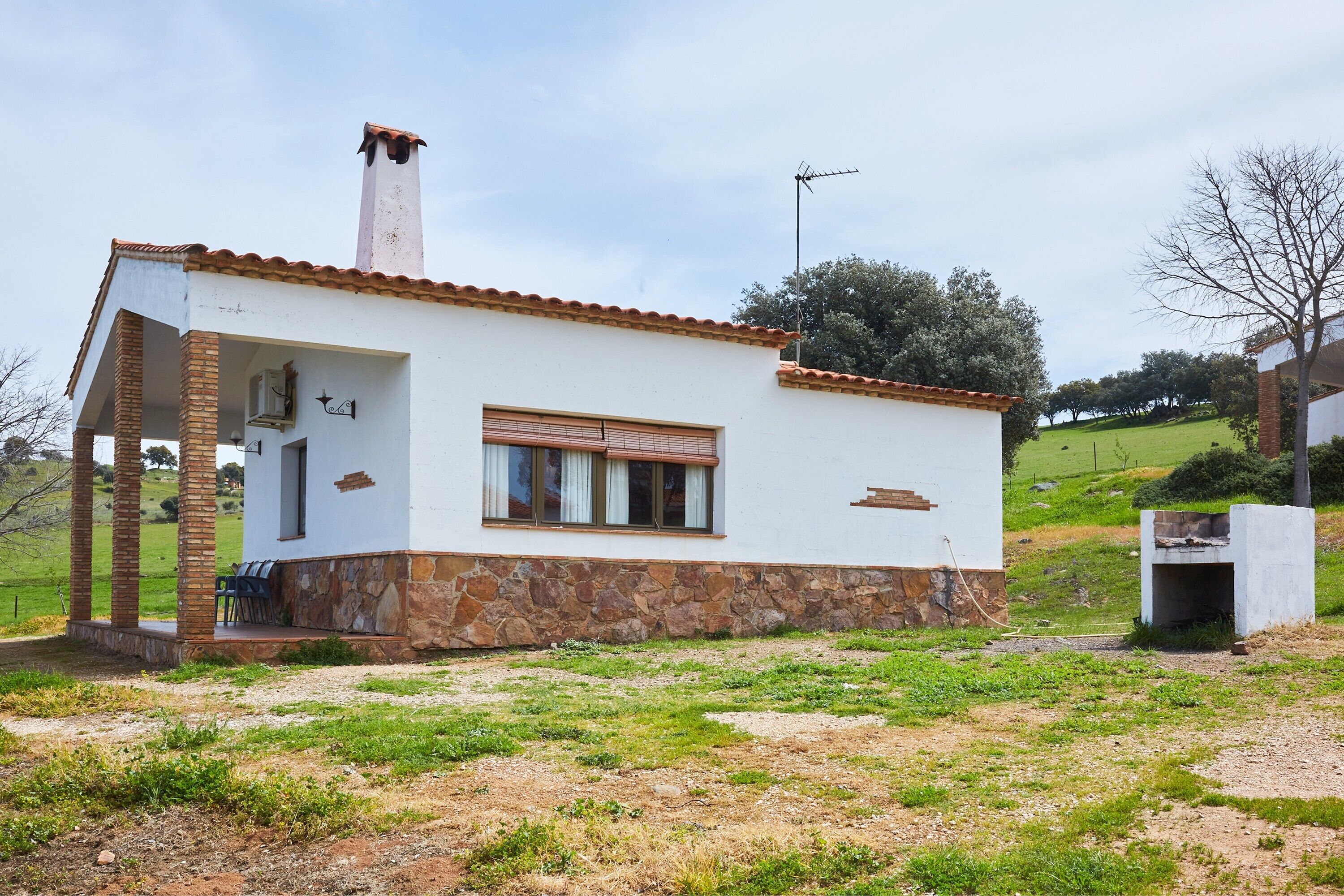 Una pequeña casa de un piso con base de piedra, techo de tejas y una chimenea.