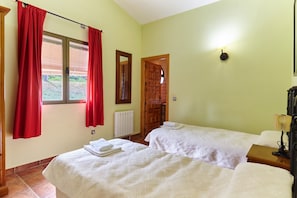 A bedroom with two beds, red curtains, a wooden door, a wall-mounted light, and a radiator. - Country House 'Casa El Collado' with Mountain View, Shared Pool and Air Conditioning (ALDEAQUEMADA)