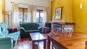 A living room with a sofa, armchair, wooden coffee table, dining table, and a fireplace. - Country House 'Casa La Encina' with Mountain View, Shared Pool and Air Conditioning (ALDEAQUEMADA)