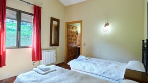 A room with two beds, a radiator, a window with red curtains, a wooden door, and a wall-mounted light fixture. - Country House 'Casa La Encina' with Mountain View, Shared Pool and Air Conditioning (ALDEAQUEMADA)