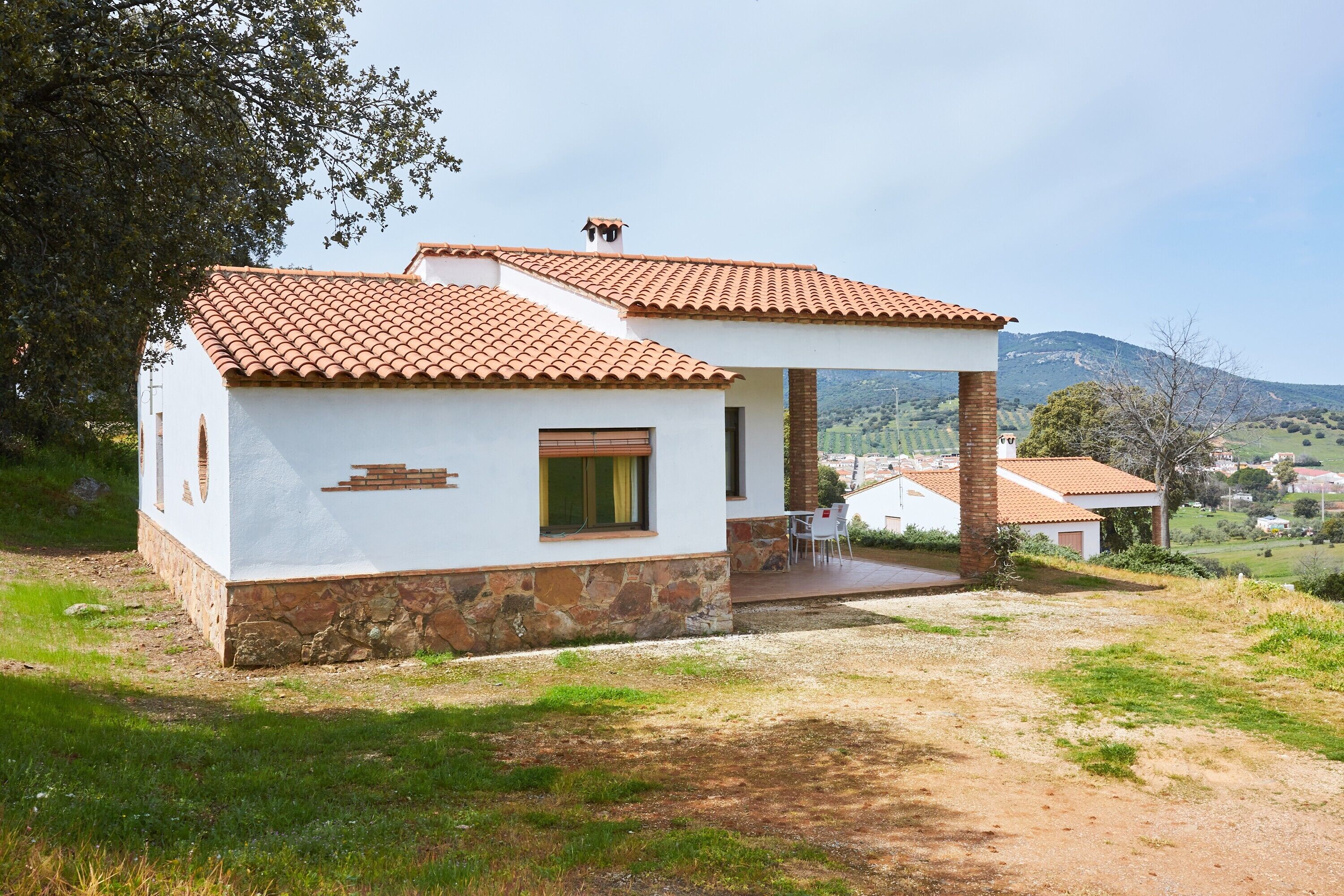 Una casa de un piso con techo de tejas, base de piedra y un pequeño porche.